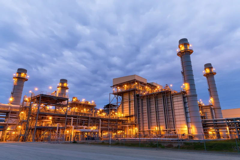 Gas turbine power plant at twilight with illuminated industrial structures and exhaust chimneys