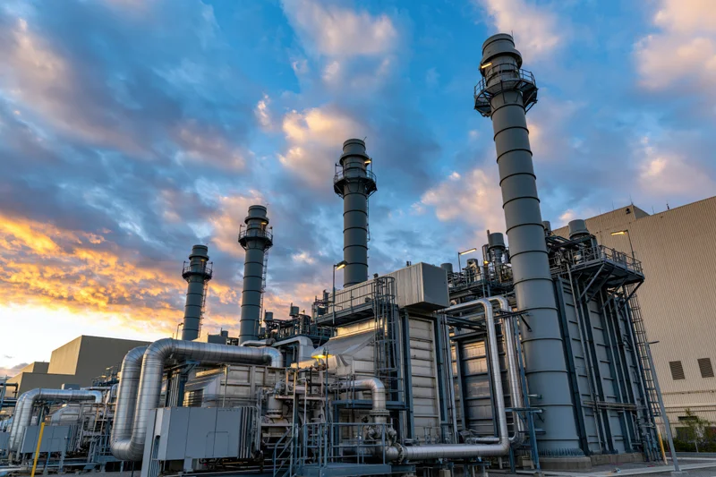 Gas turbine power plant with tall exhaust stacks and pipes under a cloudy twilight sky