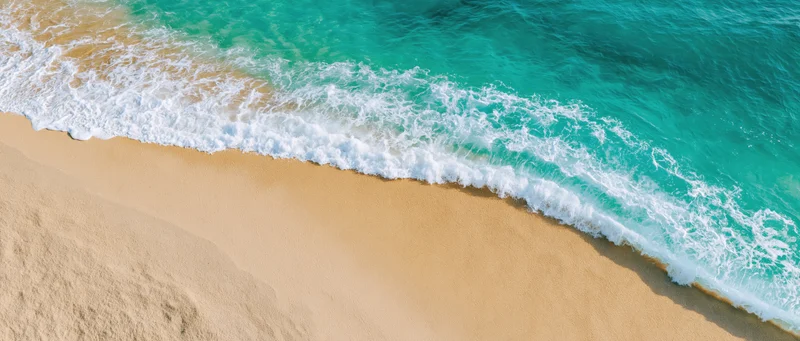 Gentle ocean wave washing over clean sandy beach from above