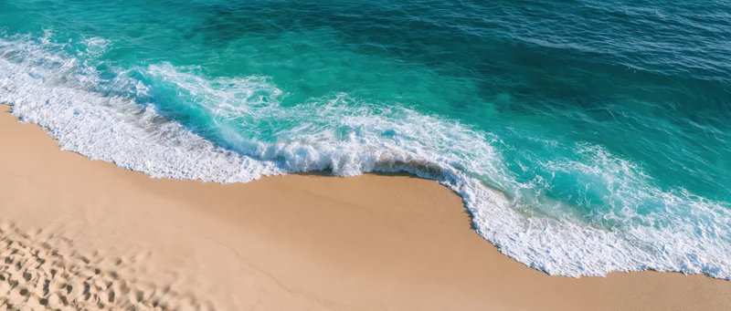 Gentle ocean wave washing over sandy beach from above