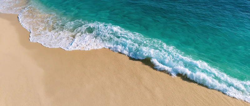 Gentle ocean wave washing over clean sandy beach from above