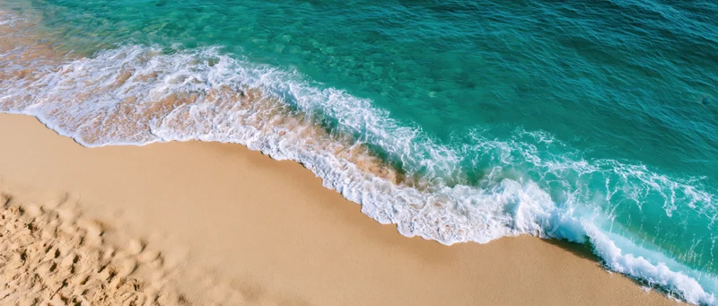 Gentle ocean wave washing over clean sandy beach from above