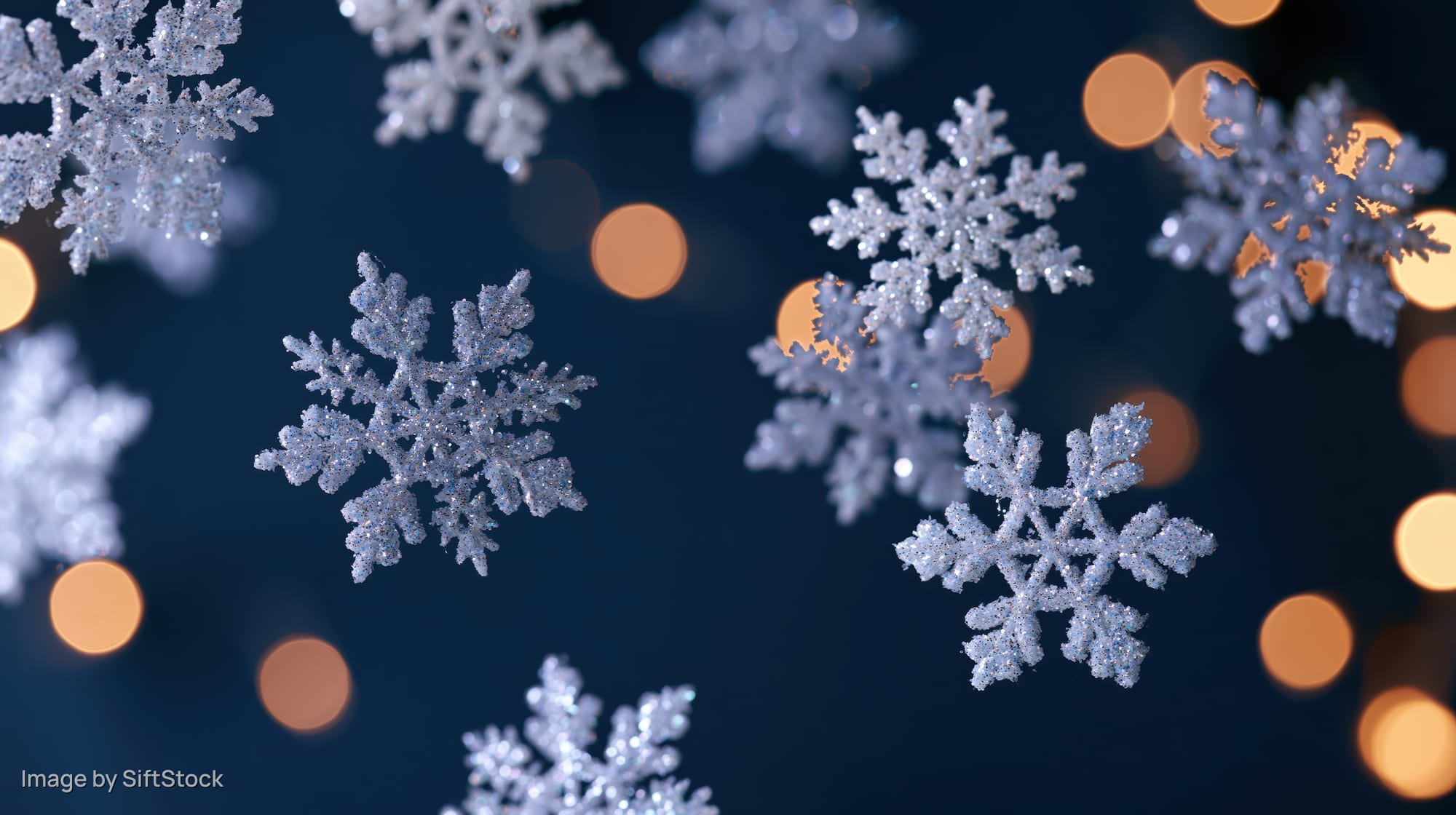 Glittery snowflakes floating against a dark blue background with warm bokeh lights