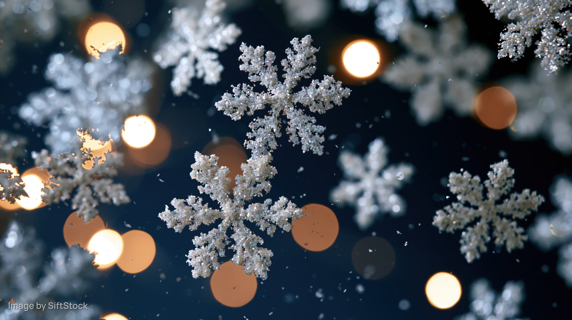 Glittery snowflakes floating against a dark blue background with warm bokeh lights