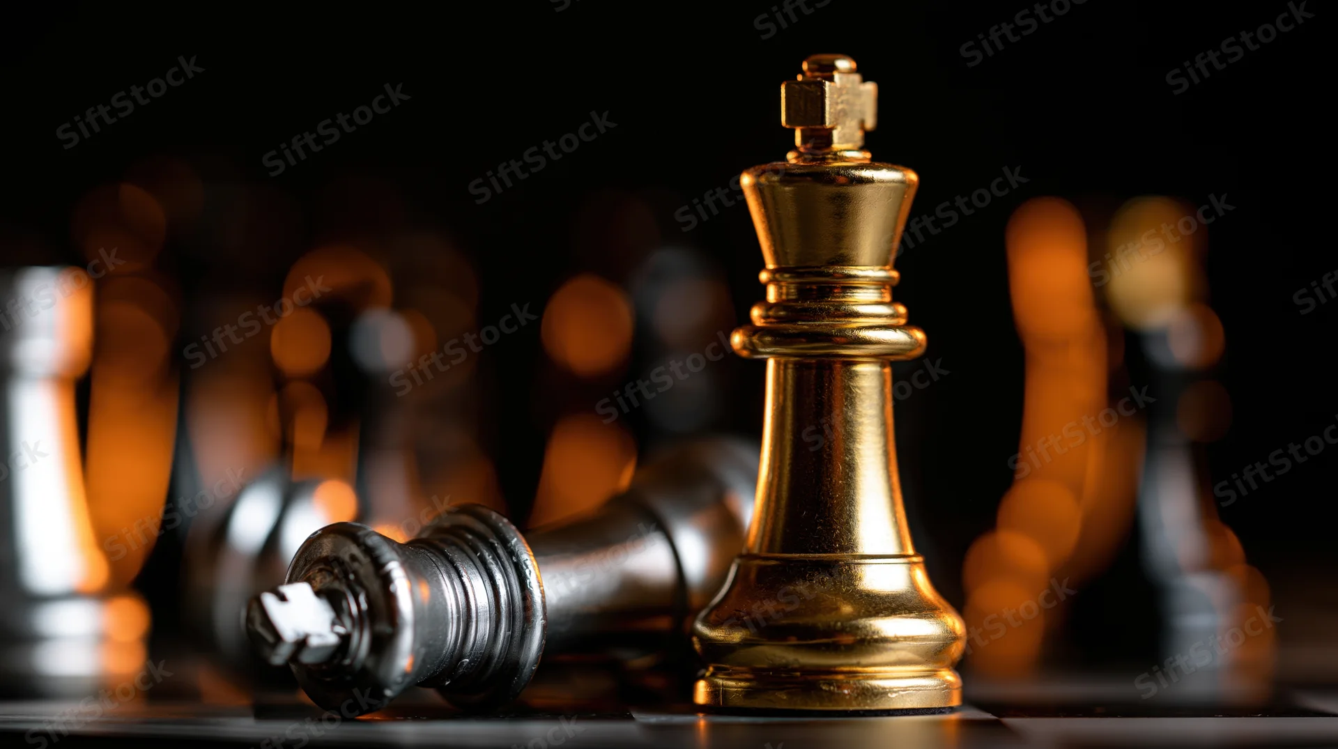 Gold chess king standing upright beside a fallen silver king on a dark board with blurred background lights