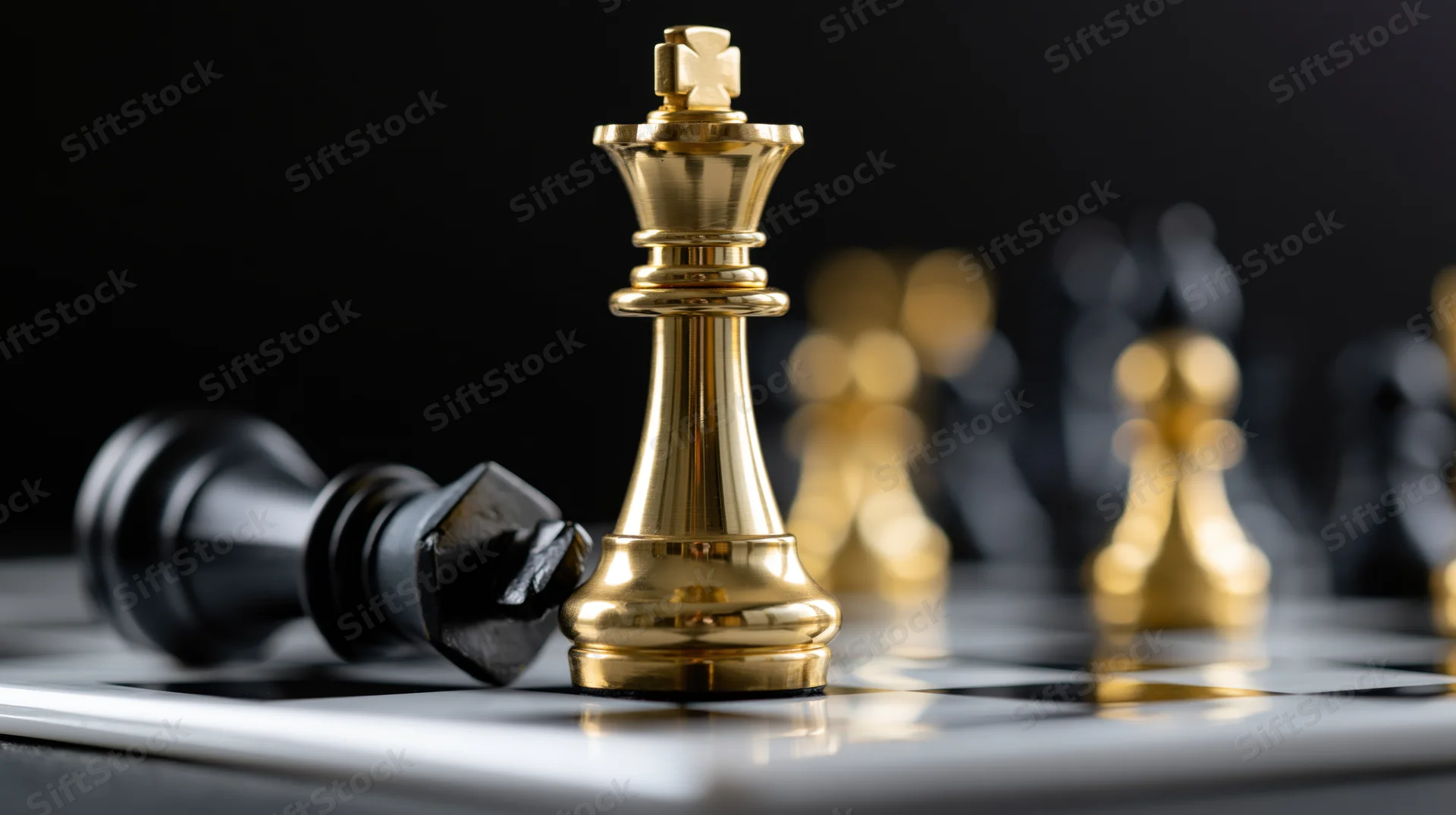 Gold chess king standing upright over fallen black king on chessboard