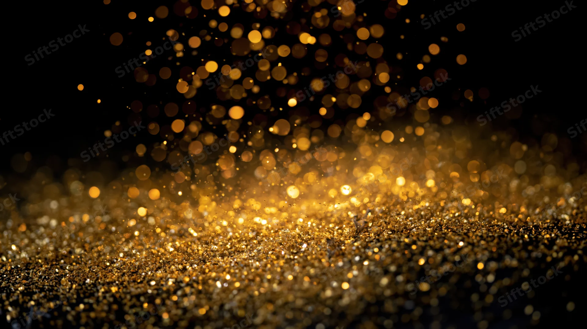 Gold glitter particles floating and falling against a dark background with bokeh light effects