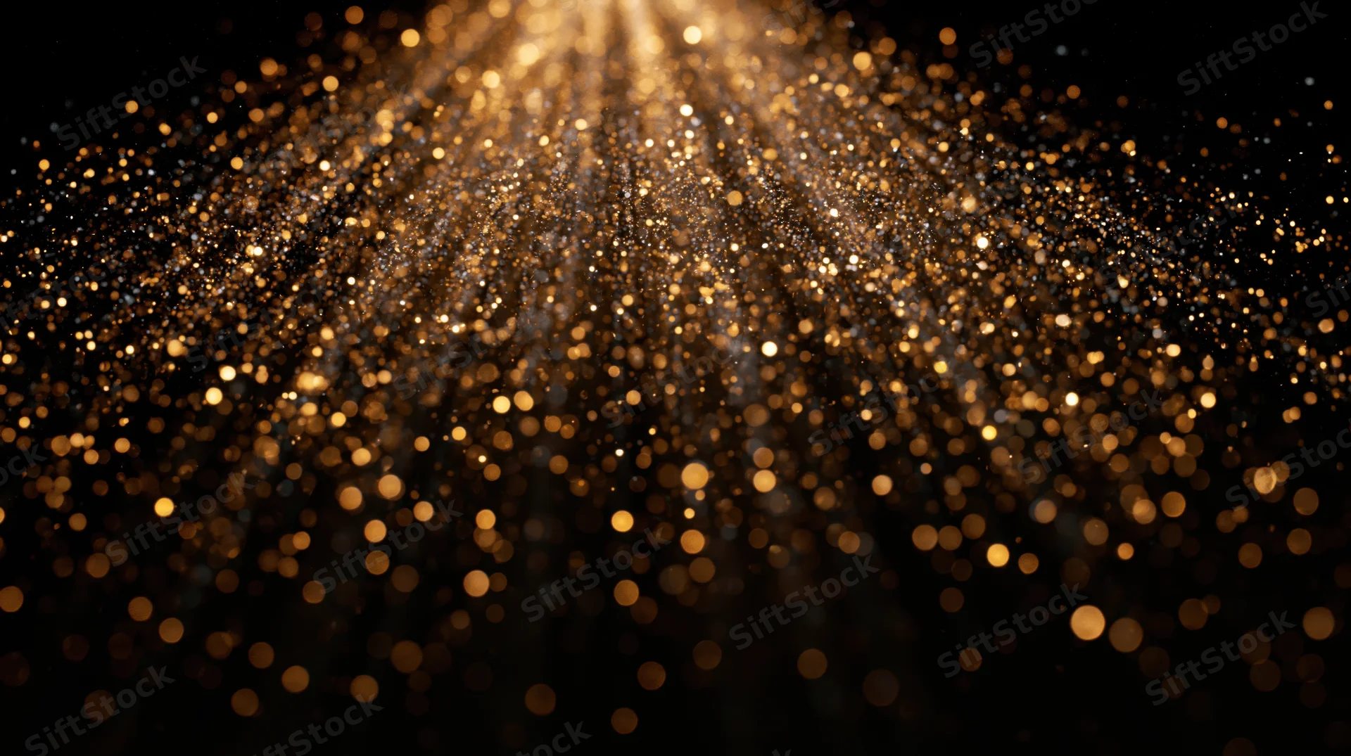 Golden dust particles floating and falling in a radiant bokeh effect against black background