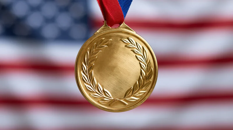 Gold medal with embossed laurel wreath hanging from red and blue ribbon against blurred american flag background