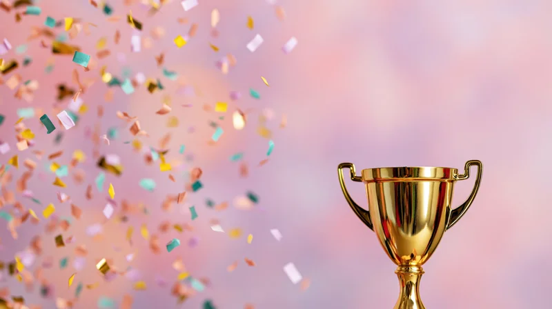 Golden trophy cup with falling confetti against a soft pink background