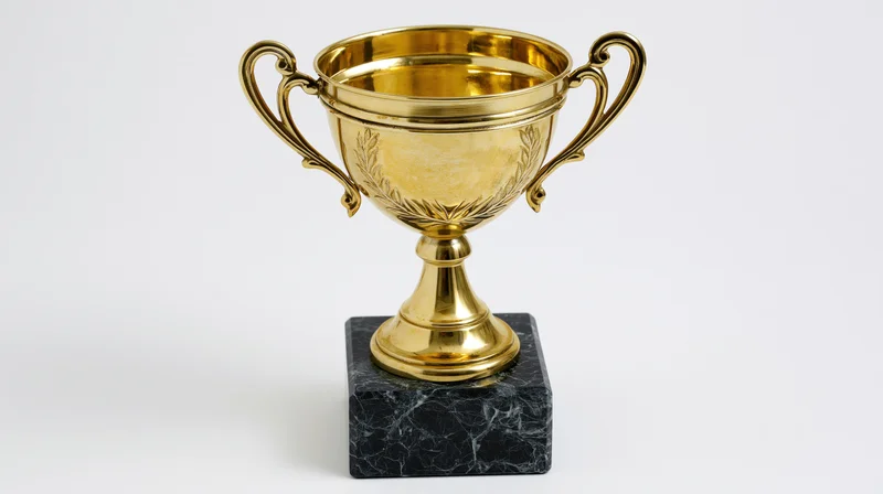 Gold trophy cup with engraved laurel wreath on black marble base against white background