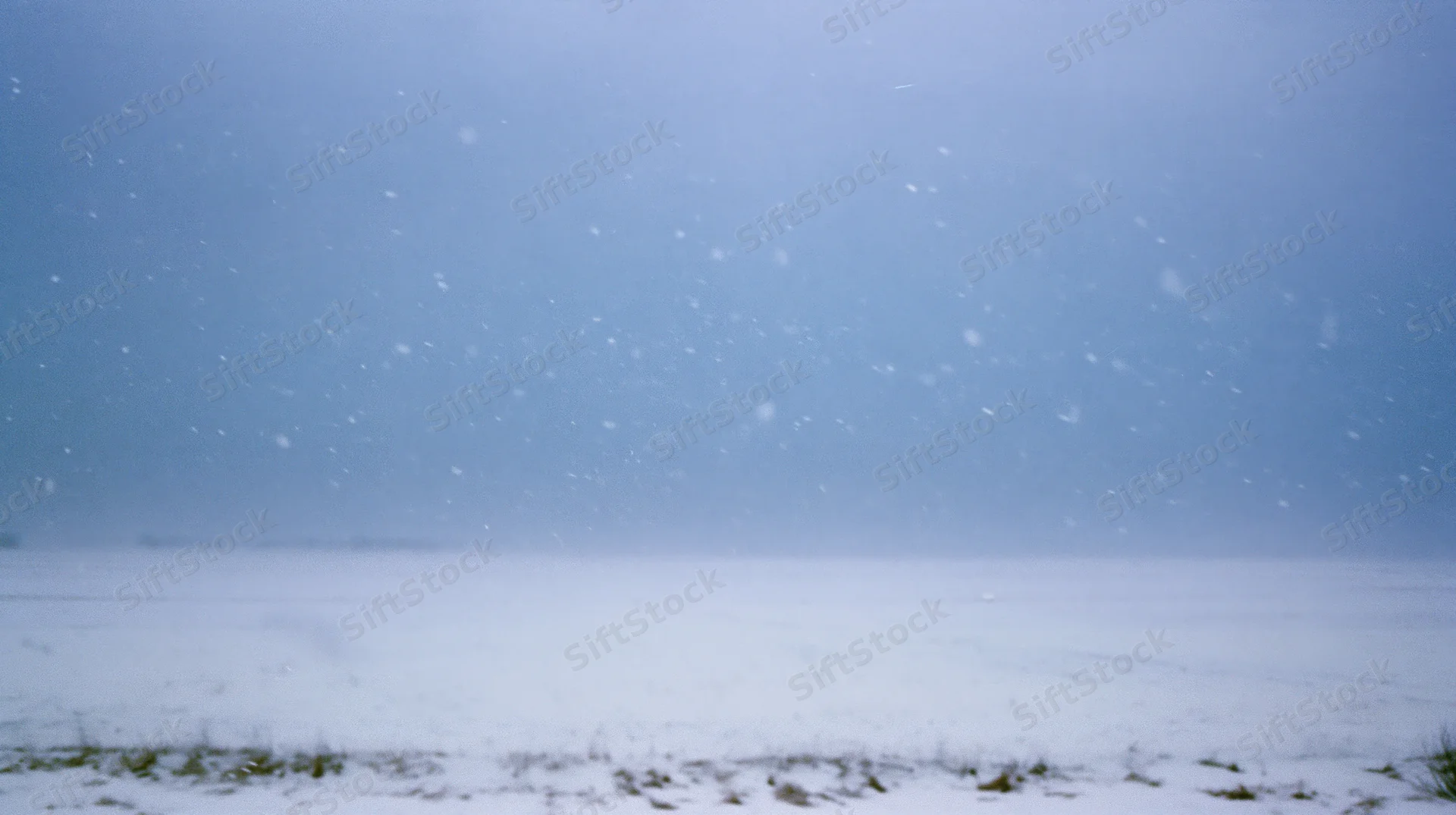 Heavy snowfall over a flat snowy field under an overcast sky