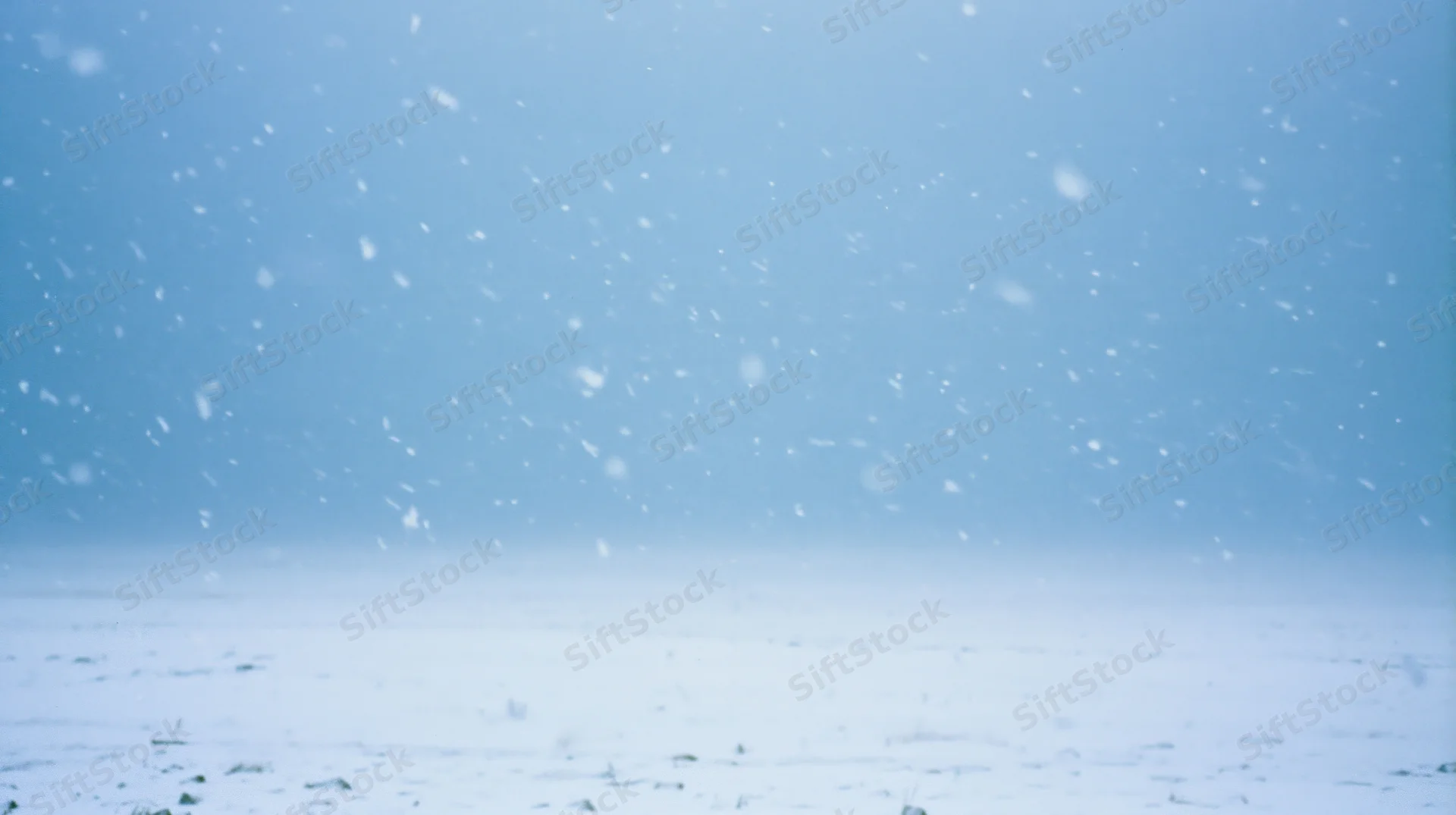 Heavy snowfall over a flat snowy landscape under a pale blue sky