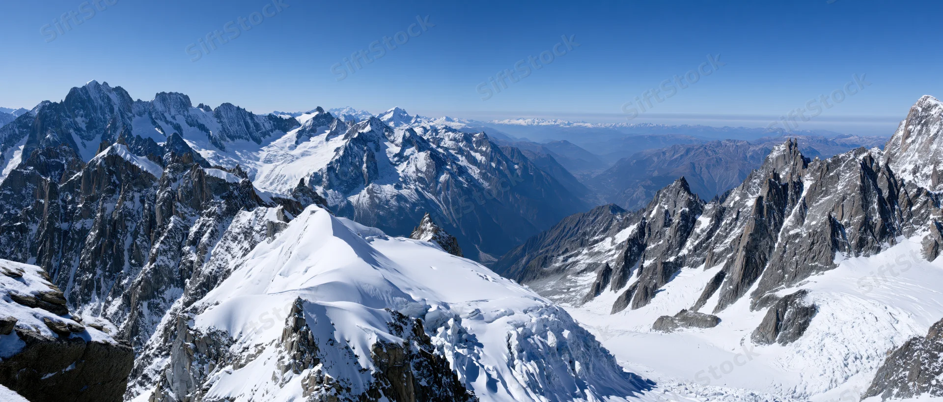 Panoramic view of snow-covered mountain peaks and valleys in the Mont Blanc massif under a clear blue sky