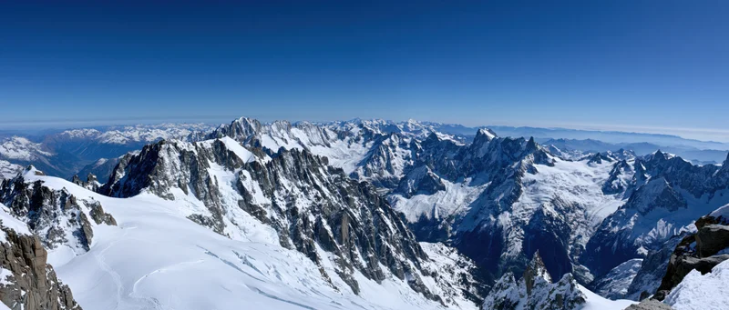 Panoramic view of snow-covered alpine peaks and glaciers under clear blue sky