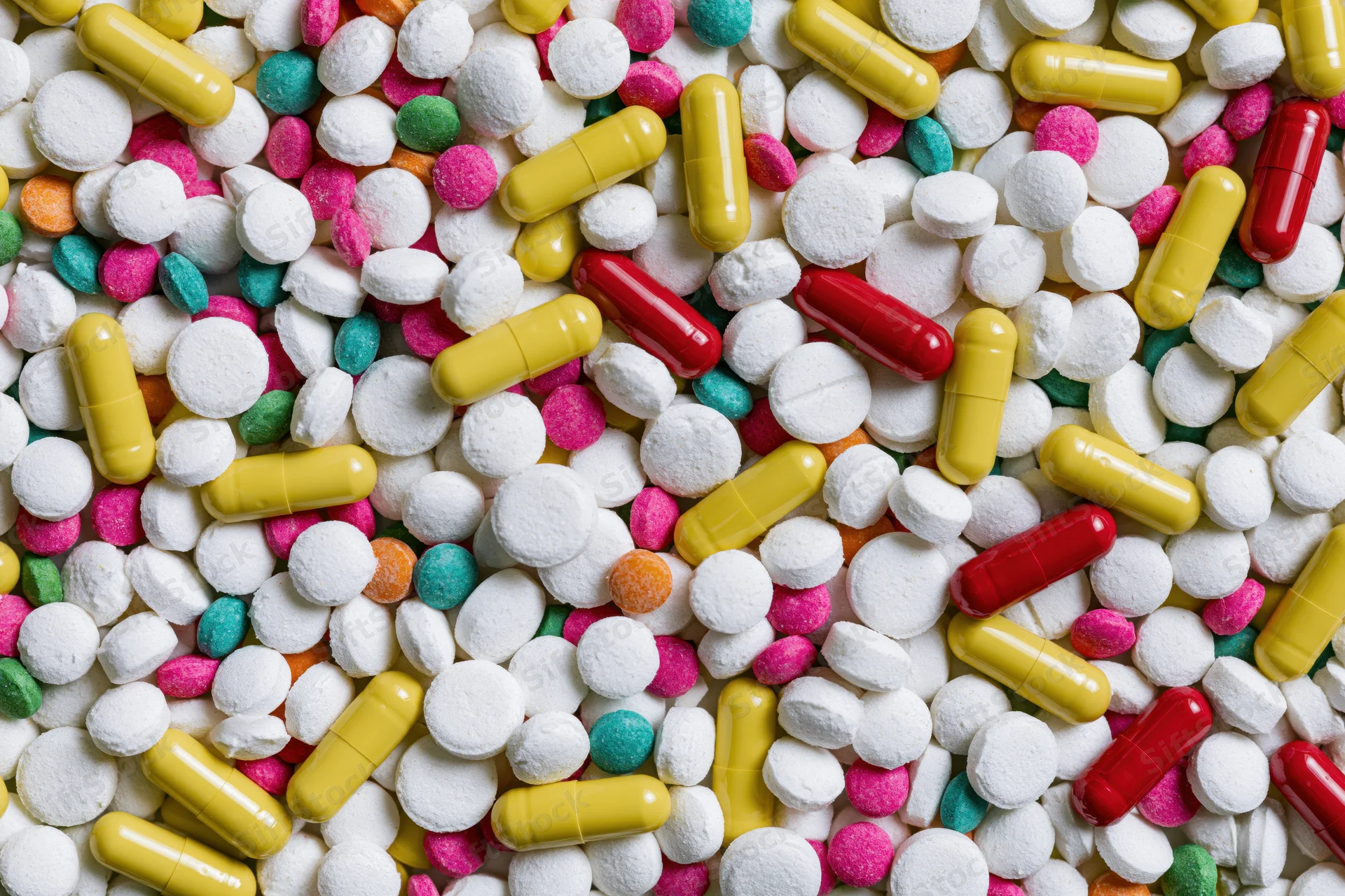 Assorted pharmaceutical pills tablets and capsules scattered in closeup top view