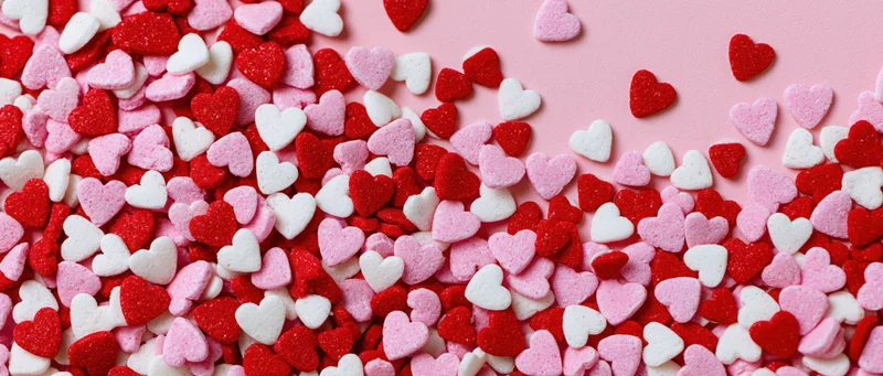 Heart-shaped sugar sprinkles scattered across a pink surface in a flat lay arrangement