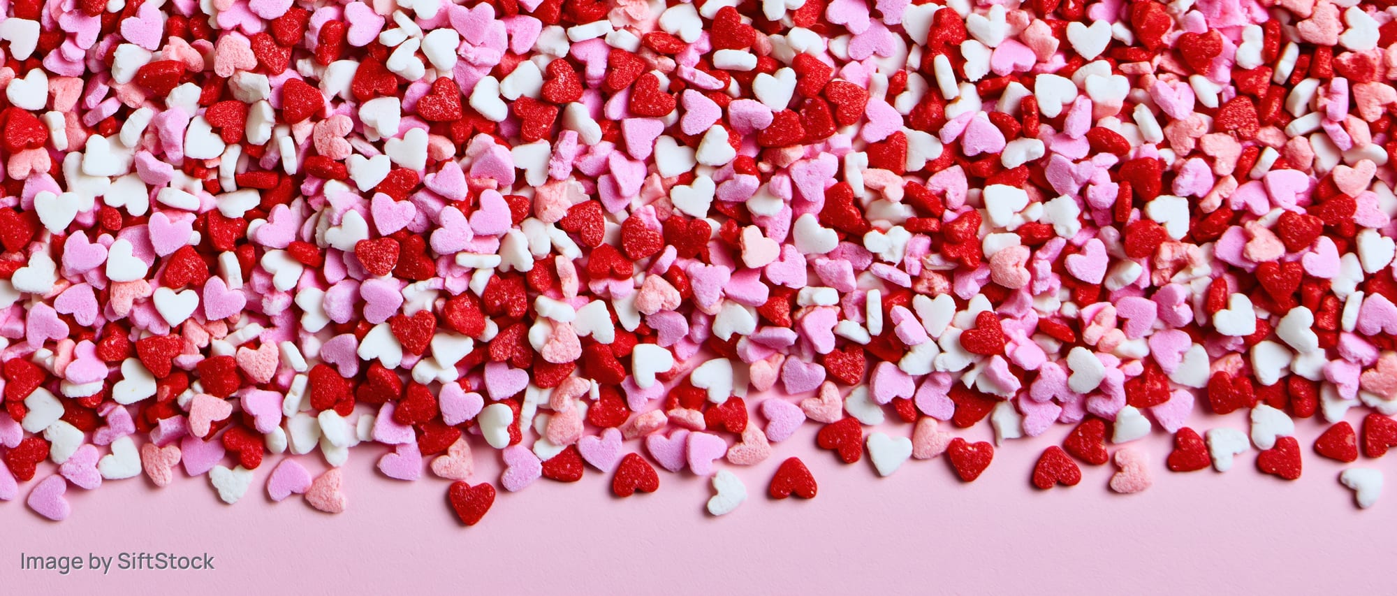Heart-shaped sugar sprinkles scattered across a pink surface