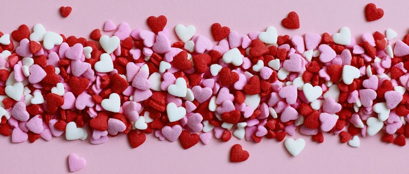Heart-shaped sugar sprinkles scattered across a pink surface in a flat lay arrangement