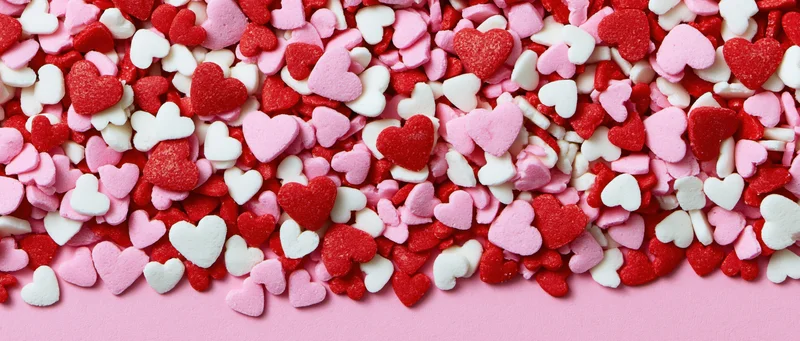 Heart-shaped sugar sprinkles scattered across a pink surface with copyspace at the bottom