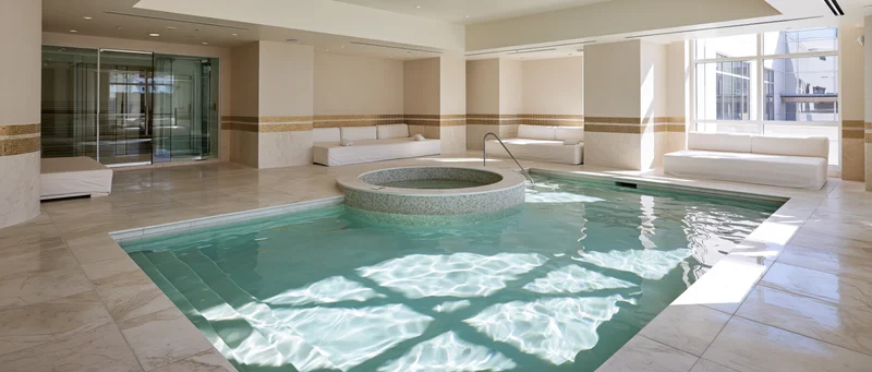 Indoor spa pool with circular hot tub and white lounge benches in a modern hotel interior