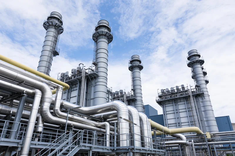 Industrial power plant with tall metal chimneys and network of pipes under a partly cloudy sky