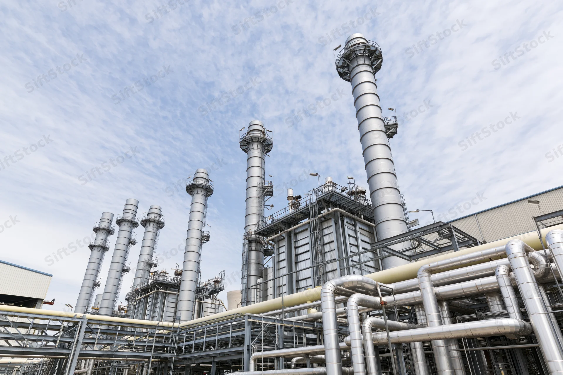 Industrial power plant with tall metal chimneys and network of pipes under a partly cloudy sky