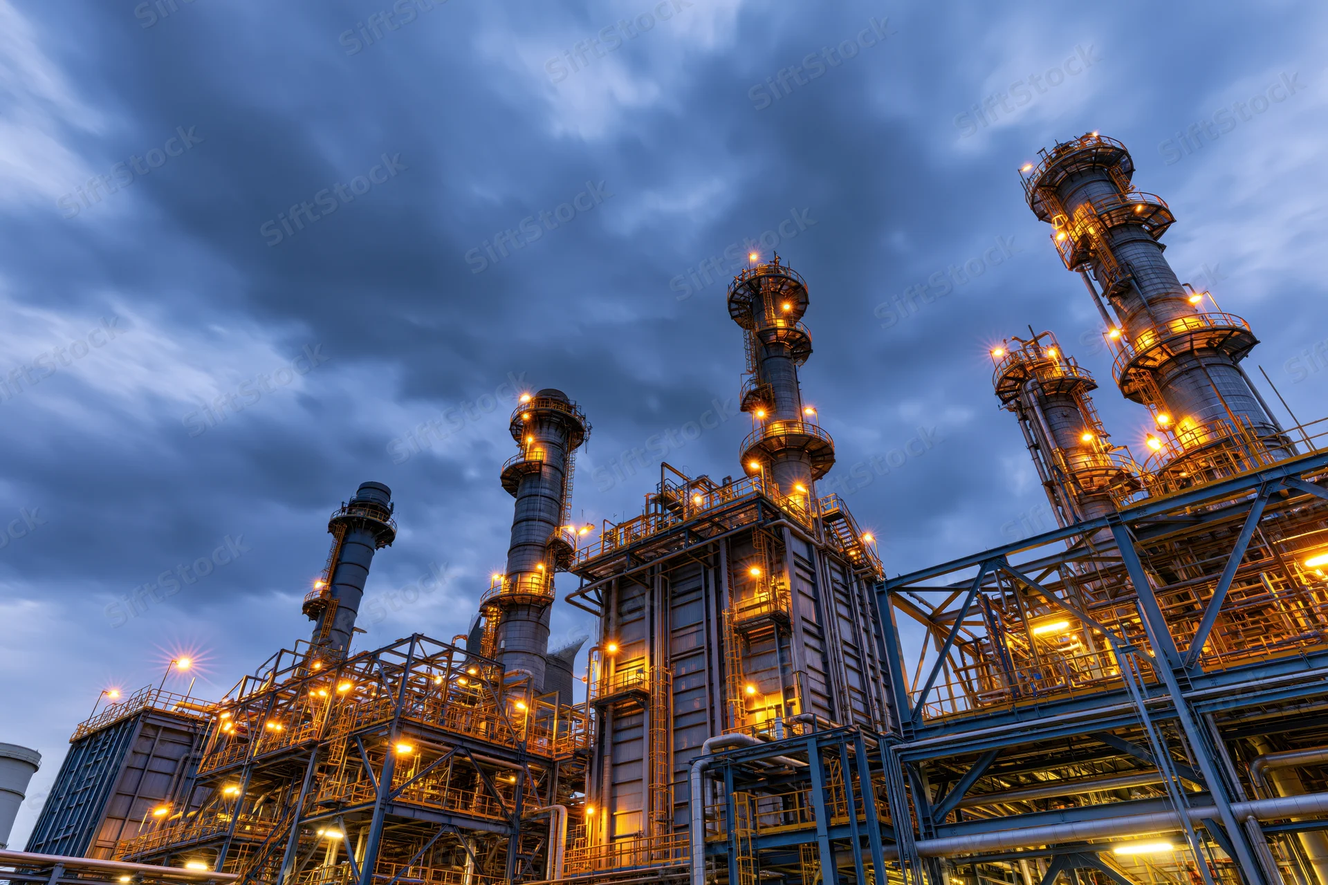 Industrial refinery towers illuminated at dusk under cloudy sky