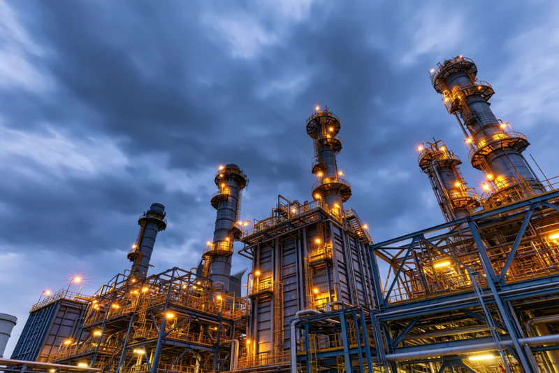 Industrial refinery towers illuminated at dusk under cloudy sky