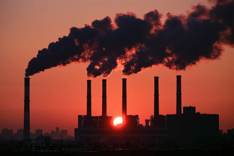 Industrial power plant with multiple smokestacks emitting dark smoke at sunset