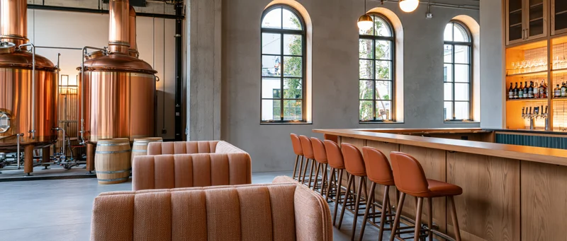 Empty craft brewery taproom interior with copper brewing stills, wooden bar, and arched windows