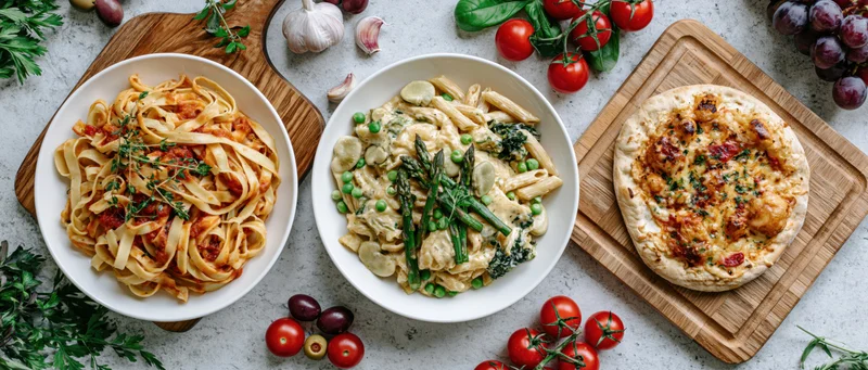 Italian food spread with pasta dishes and focaccia on wooden boards and concrete surface