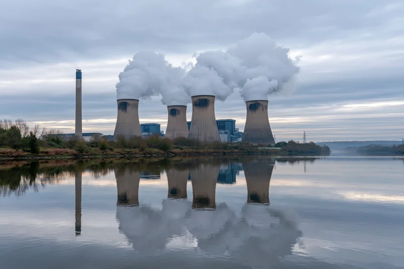 Coal-fired power plant with four cooling towers emitting steam, reflected in calm river water