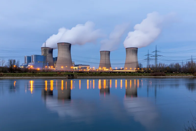 Coal power plant with four cooling towers emitting steam at twilight, reflected in a calm river