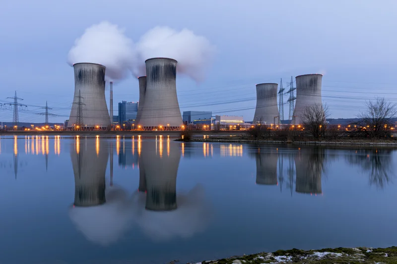 Cooling towers emitting steam at twilight reflected in calm water near a power plant