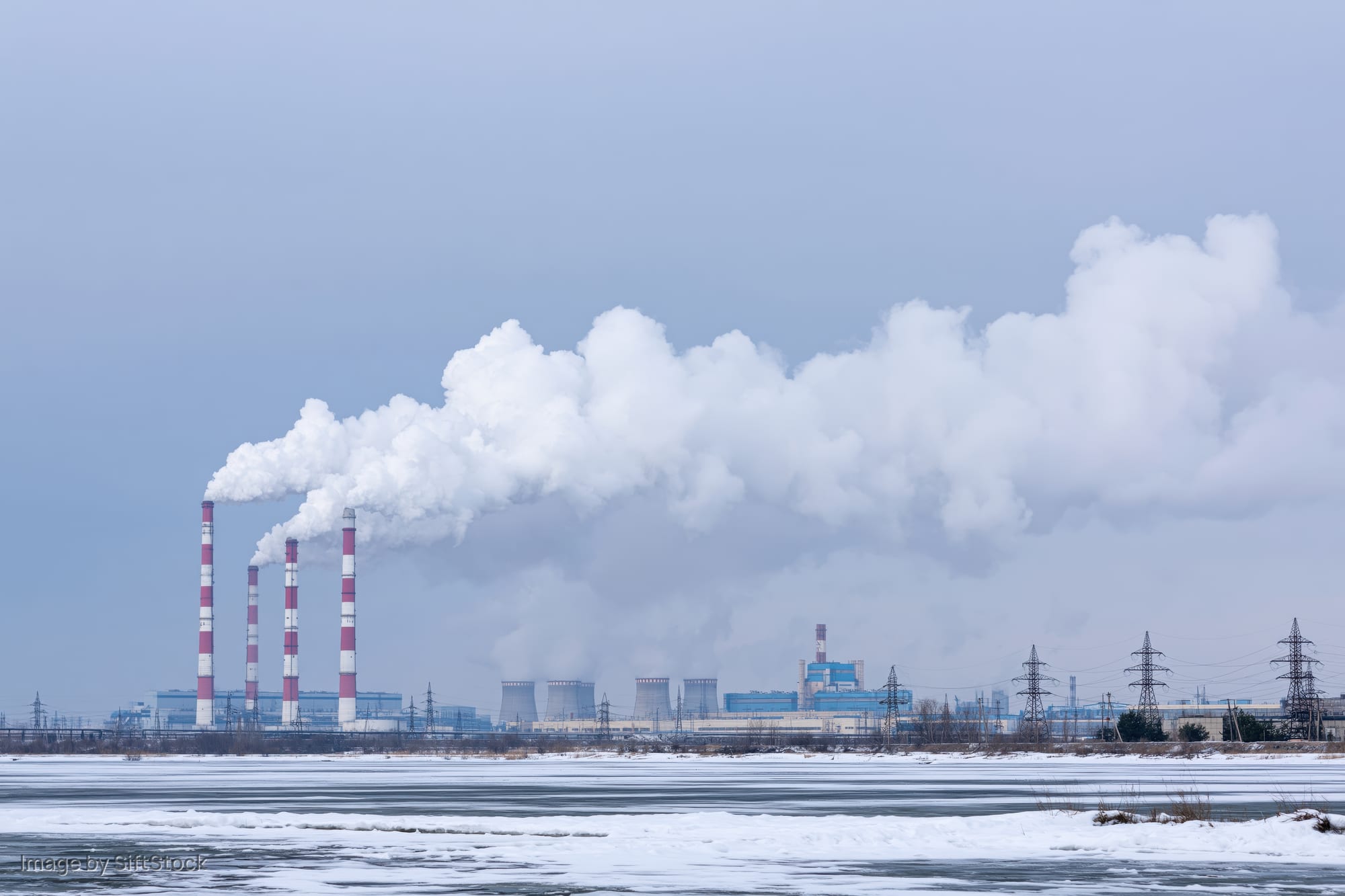 Coal power plant emitting smoke from tall red-and-white striped chimneys beside a frozen river