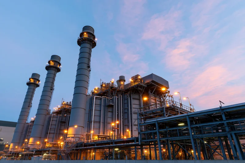 Large gas turbine power plant with tall exhaust stacks illuminated at dusk
