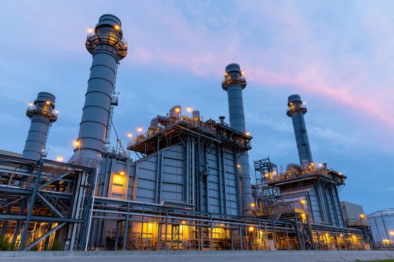 Large gas turbine power plant with tall exhaust stacks at dusk