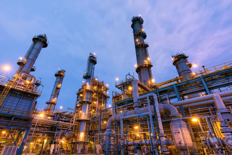 Oil refinery complex with tall towers and illuminated pipes at dusk