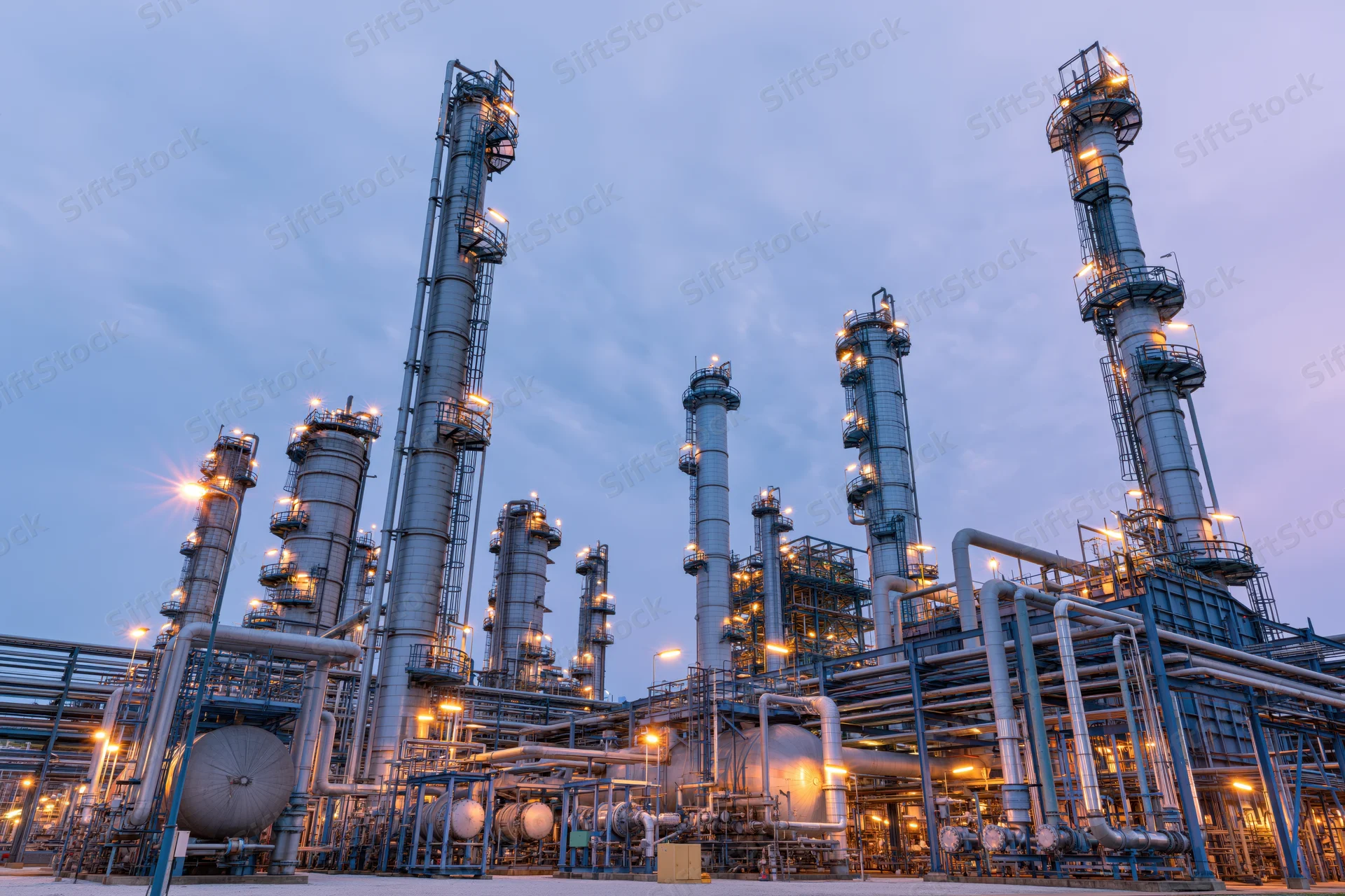 Large oil refinery complex with tall towers and pipelines illuminated at twilight