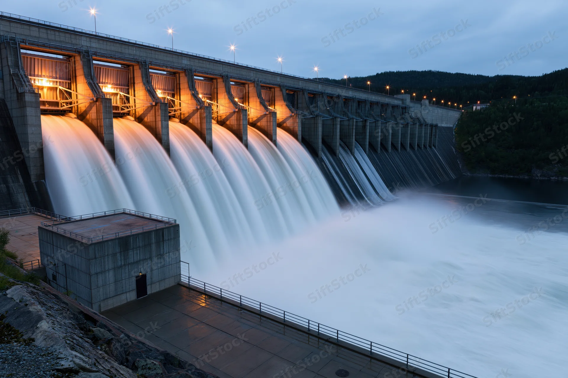 Large hydroelectric dam releasing water through multiple spillways at twilight