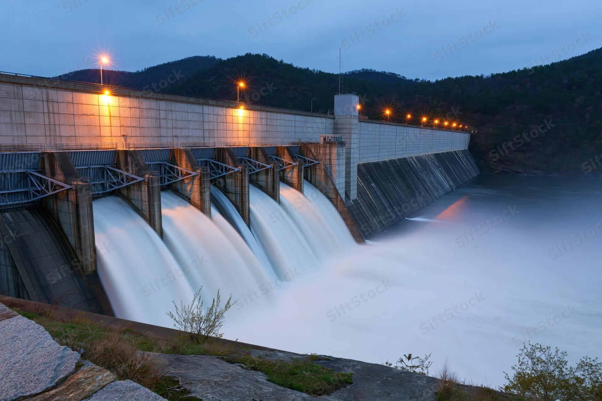 Hydroelectric dam releasing water through multiple spillways at twilight