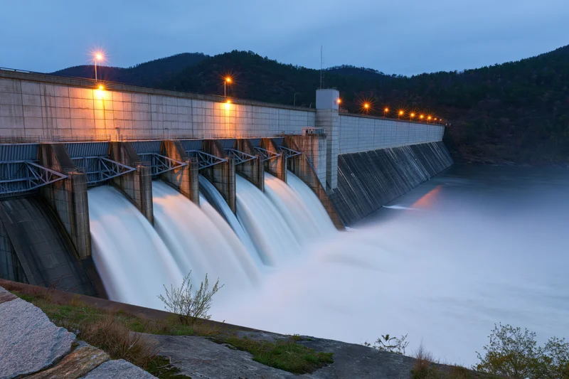 Hydroelectric dam releasing water through multiple spillways at twilight