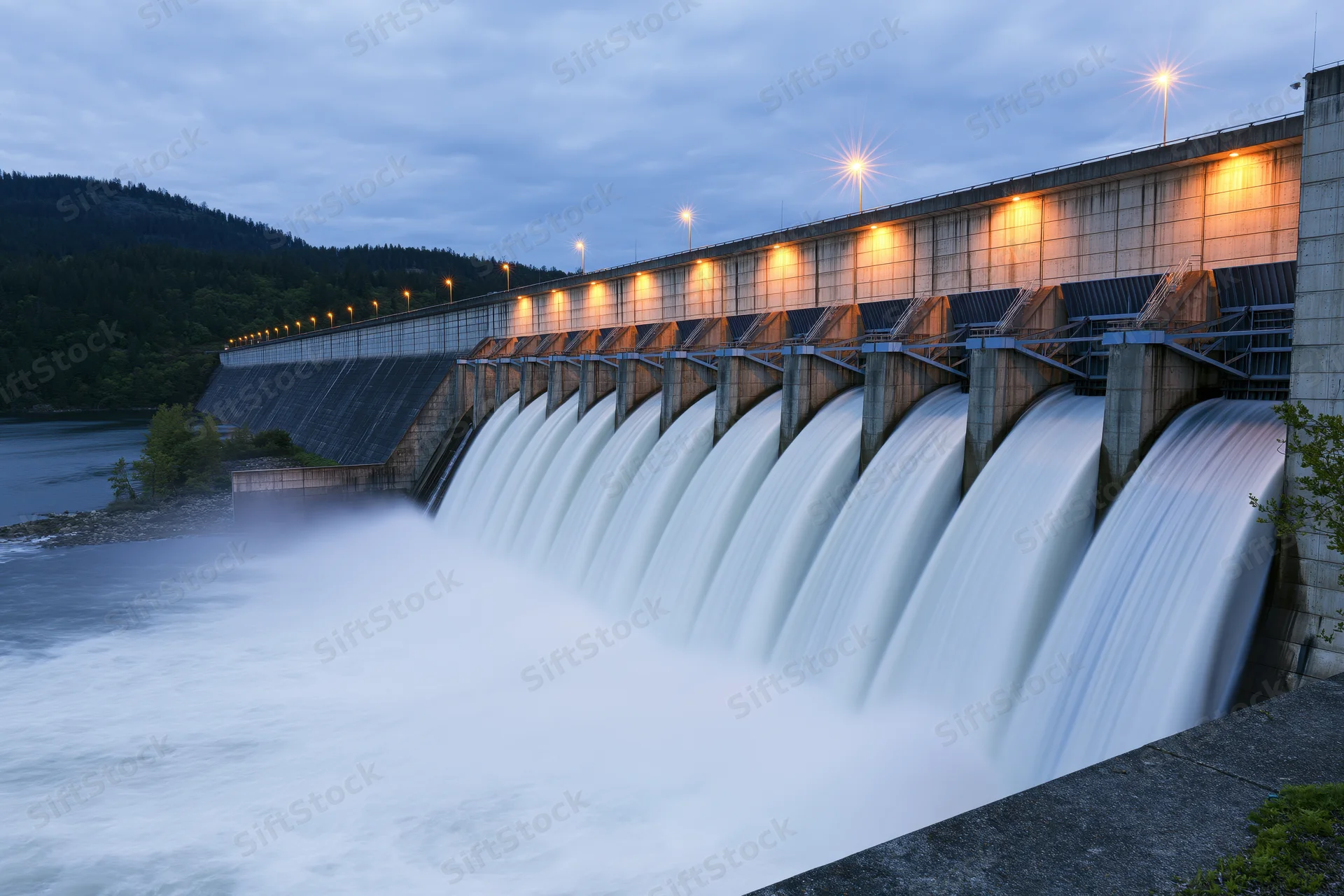Large hydroelectric dam releasing water through multiple spillways at twilight