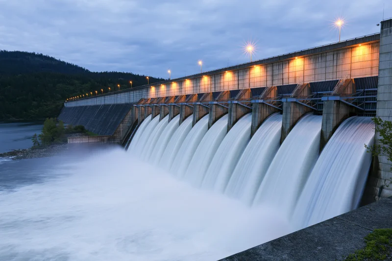 Large hydroelectric dam releasing water through multiple spillways at twilight