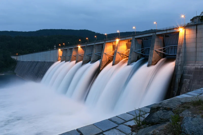 Large hydroelectric dam releasing water through multiple spillways at twilight