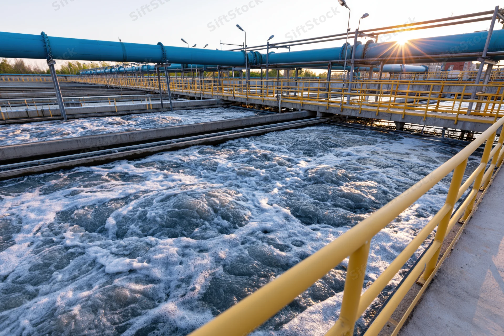 Aeration tank in wastewater treatment plant with foamy water and blue pipes at sunrise