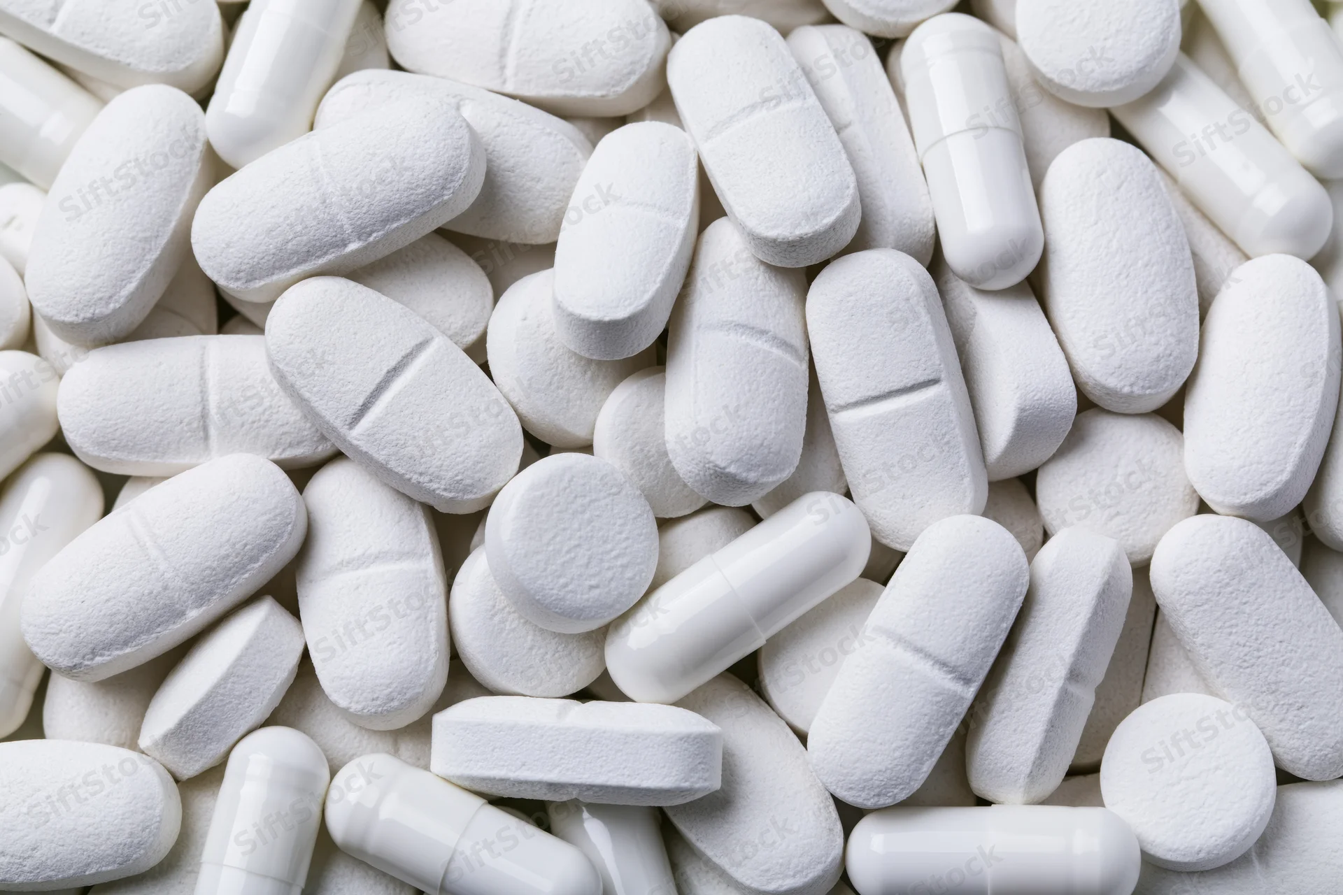 Close-up of assorted white pharmaceutical tablets and capsules piled together