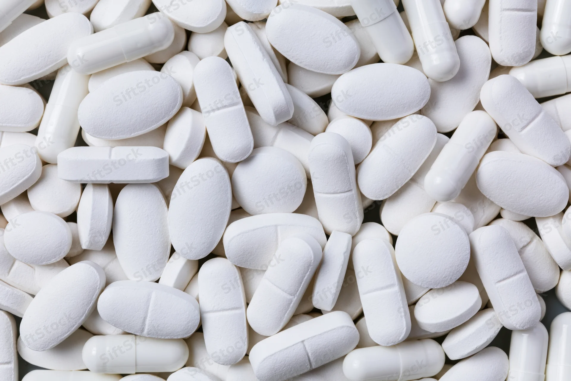 Close-up of assorted white pharmaceutical tablets and capsules piled together