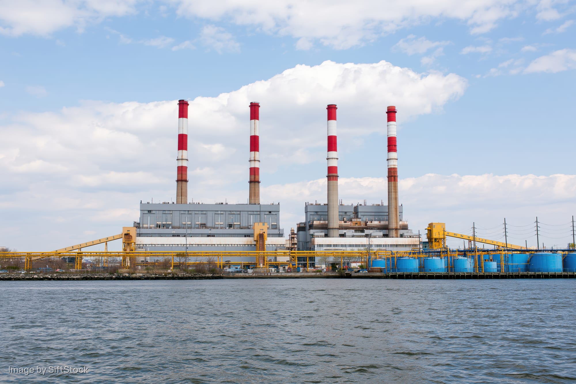 Large power plant with red-and-white smokestacks along a riverbank